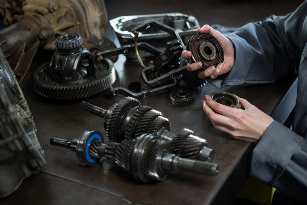 Technician inspecting industrial gears and mechanical spare parts on a workbench.